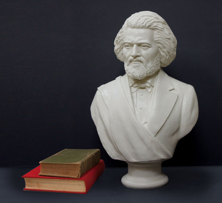 Photo of white plaster cast sculpture bust of Frederick Douglass with beard and in suit coat with toga over one shoulder and a green book stacked atop a red book beside it on dark gray background