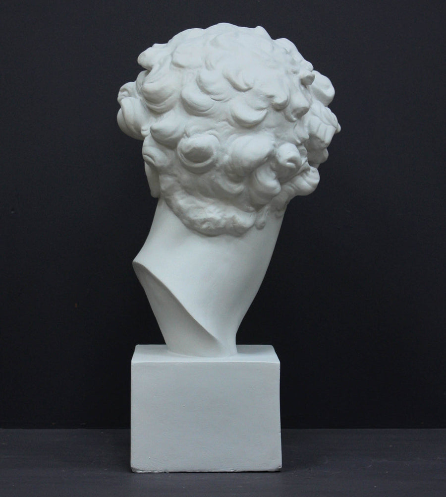 photo of back of white plaster cast bust sculpture of male with curly hair atop cube base against gray background