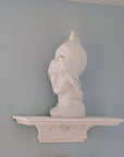 photo of white plaster cast sculpture bust of female head, namely the goddess Athena, wearing a helmet and placed on a matching white ornamental floating shelf on light blue wall