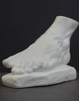 photo of white plaster cast sculpture of left foot on base against gray background