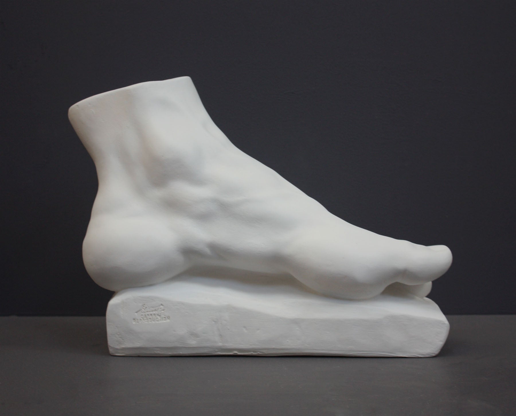 photo of white plaster cast sculpture of left foot on base against gray background