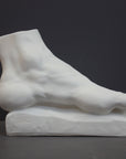 photo of white plaster cast sculpture of left foot on base against gray background