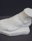 photo of white plaster cast sculpture of left foot on base against gray background