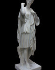 photo of white plaster cast of female figure, namely the goddess Diana, in robes about to clasp two pieces together at proper right shoulder, against black background