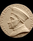 photo of off-white plaster cast relief sculpture of small medallion of male portrait in profile, namely Cosimo de Medici, and text around the edge on black background