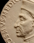 detail photo of off-white plaster cast relief sculpture of small medallion of male portrait in profile, namely Cosimo de Medici, and text around the edge on black background