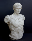 photo of white plaster cast sculpture of a man's torso with armor and robes with his right arm raised, namely Augustus Caesar, against a gray background