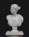 photo of white plaster cast bust sculpture of woman, namely the goddess Diana, with drapery and crown and up-do set atop a short white plaster cast pedestal in the Doric style with a fluted column against a gray background