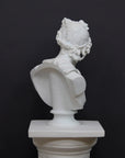 back view photo of white plaster cast bust sculpture of man, namely the god Apollo, with hair piled high in the front and a broach near his neck holding robes set atop a white pedestal against a gray background