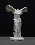 photo of white plaster cast sculpture of winged, headless female figure with flowing drapery on a gray background
