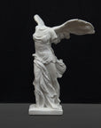 photo of white plaster cast sculpture of winged, headless female figure with flowing drapery on a gray background