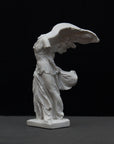 photo of white plaster cast sculpture of winged, headless female figure with flowing drapery on a gray background