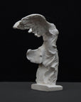 photo of white plaster cast sculpture of winged, headless female figure with flowing drapery on a gray background