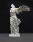 photo of white plaster cast sculpture of winged, headless female figure with flowing drapery on a gray background