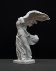 photo of white plaster cast sculpture of winged, headless female figure with flowing drapery on a gray background