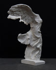 photo of white plaster cast sculpture of winged, headless female figure with flowing drapery on a gray background