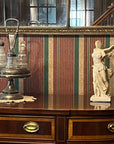 photo of off-white plaster cast sculpture of winged, headless female figure with flowing drapery atop brown antique buffet with wall mirror behind and striped wallpaper behind