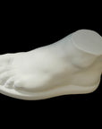photo of white plaster cast sculpture of male foot on panel against black background