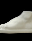 photo of white plaster cast sculpture of male foot on panel against black background