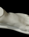 photo of white plaster cast sculpture of male foot on panel against black background