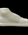 photo of white plaster cast sculpture of male foot on panel against black background