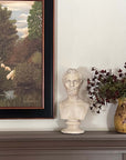 plaster cast bust sculpture of man with beard, namely Lincoln, on mantel beside cream-colored jar holding small red flowers and folk art painting of animals on white wall behind