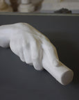 photo of white plaster cast of right hand grasping a staff or pole against gray surface with white plaster cast sculptures visible in background