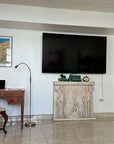 photo of plaster cast of free-standing relief sculpture with three female figures, two of which are caryatides, against a living room wall with a television mounted above it and wooden desk and other decor nearby