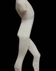 photo of white plaster cast sculpture reproduction of human form in blocked manner standing in contrapposto against black background