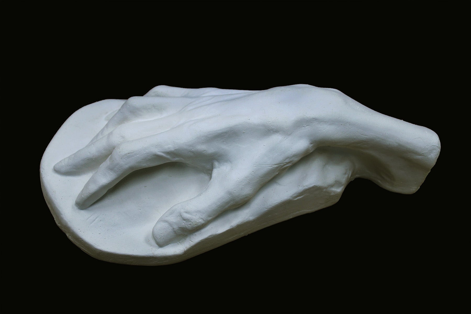 Photo of a white plaster cast of an elderly hand on a black background