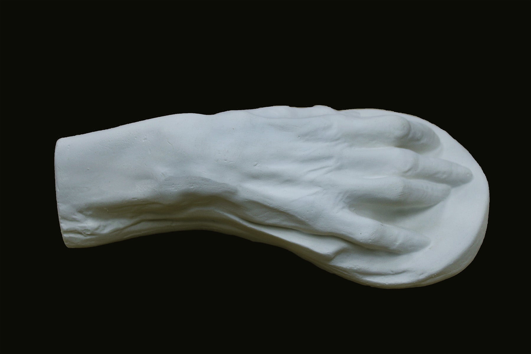 Photo of a white plaster cast of an elderly hand on a black background