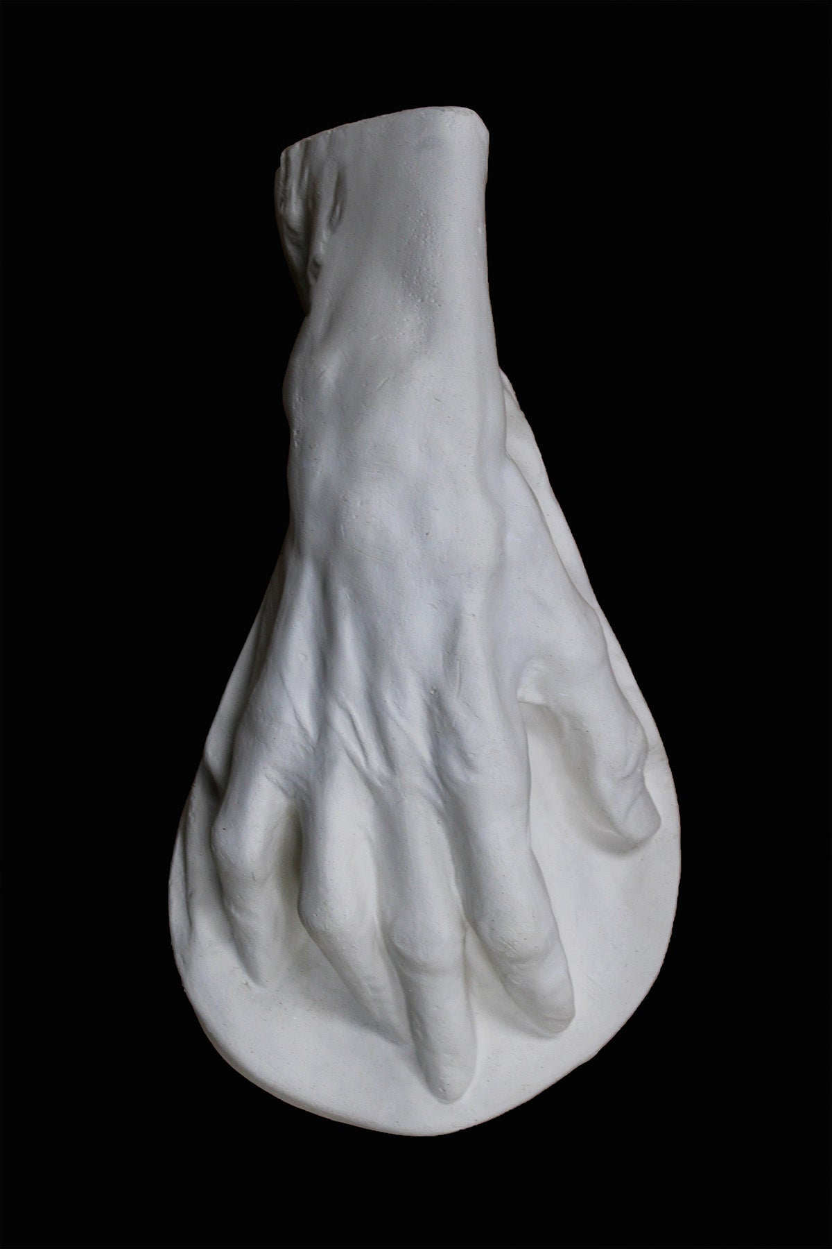 Photo of a white plaster cast of an elderly hand on a black background