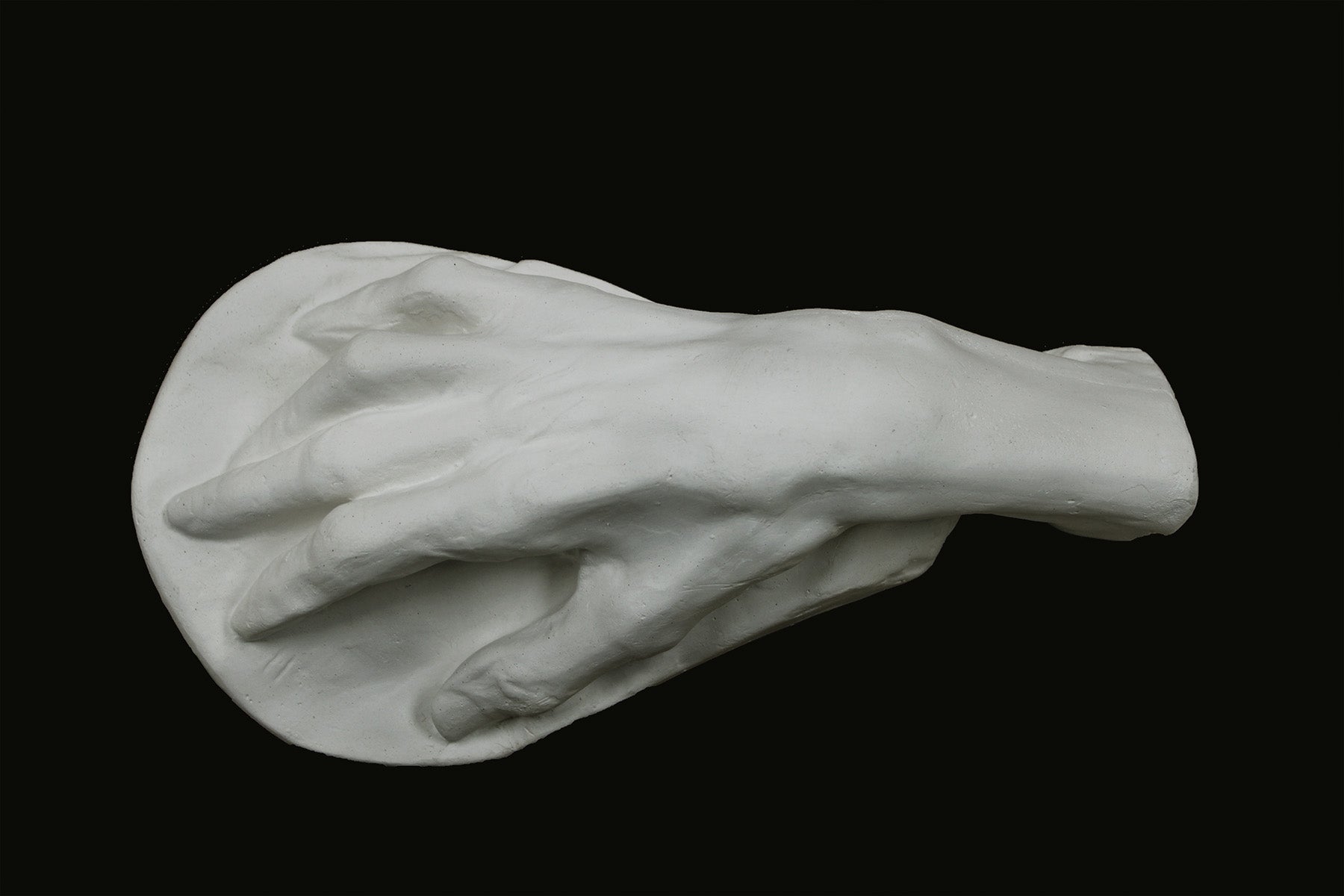 Photo of a white plaster cast of an elderly hand on a black background