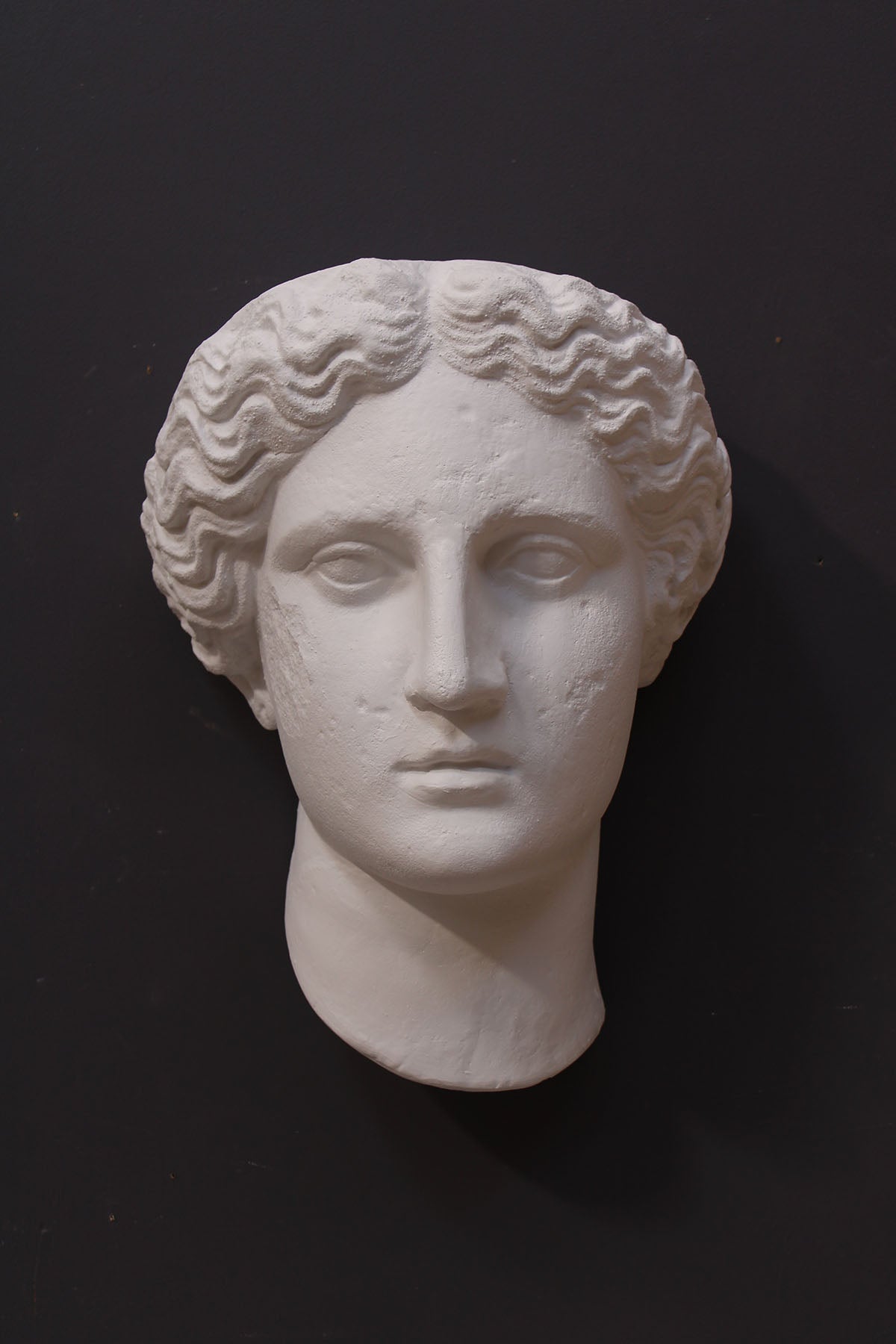 image of plaster cast sculpture mask of female, namely Athena, on a gray background