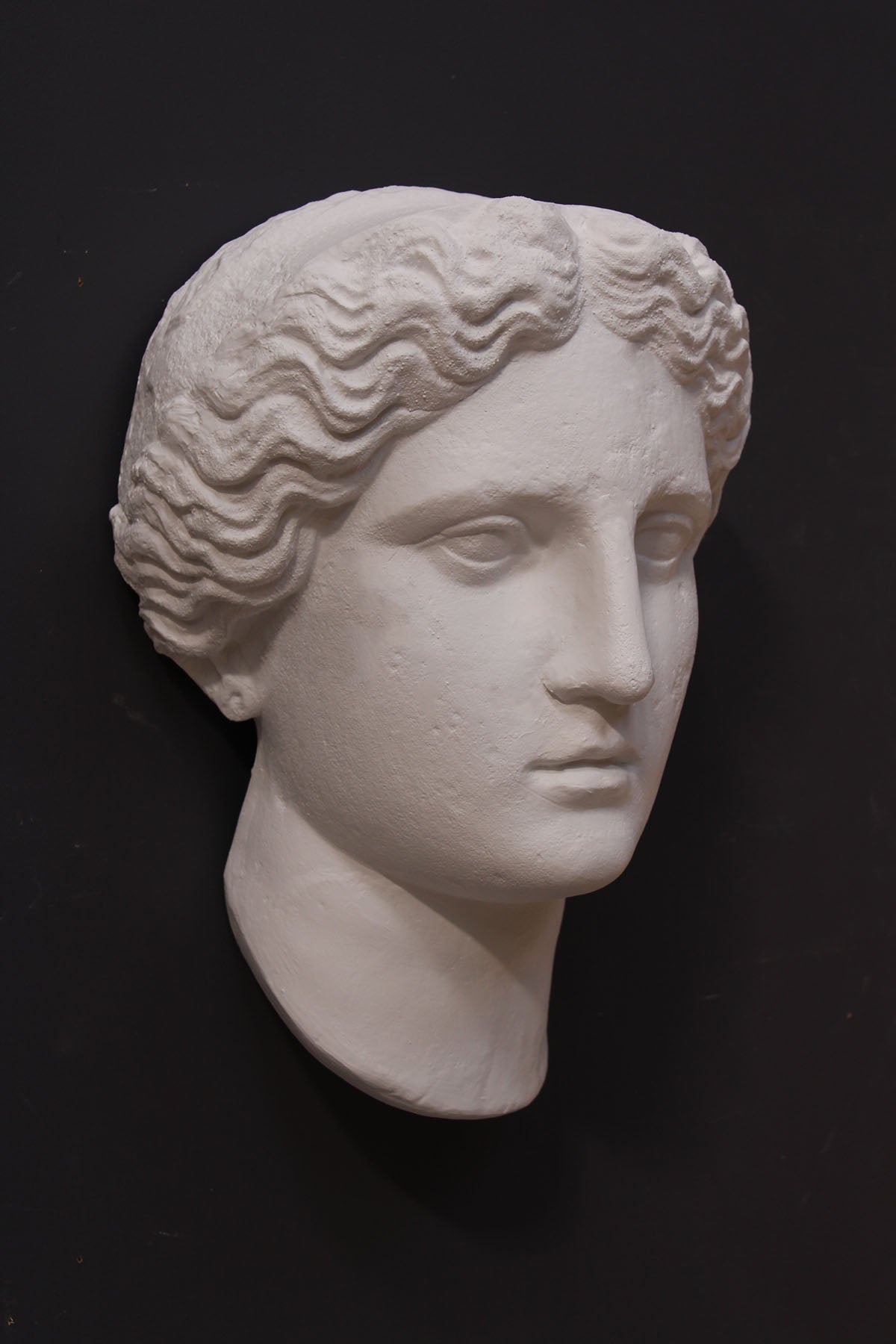 image of plaster cast sculpture mask of female, namely Athena, on a gray background