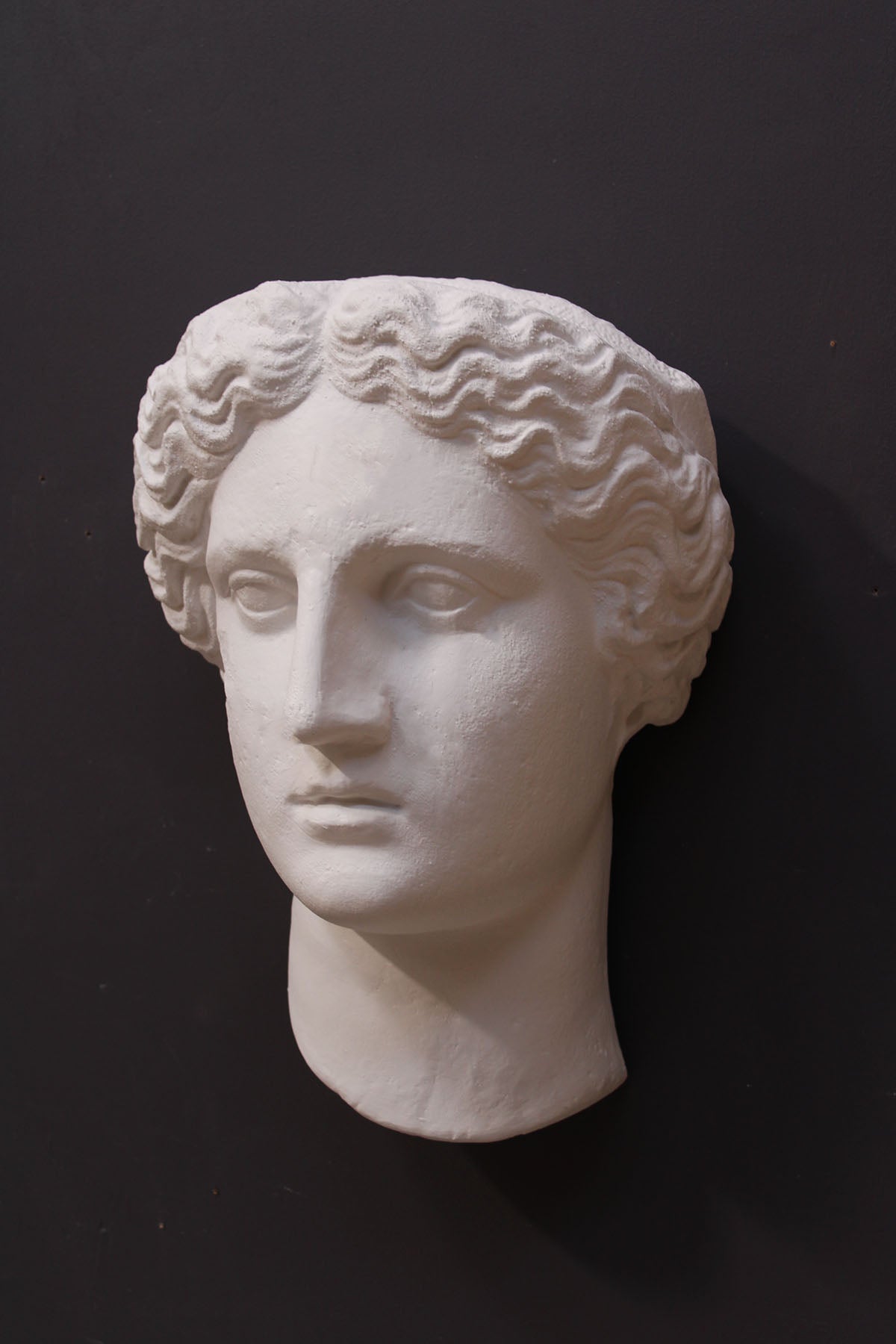image of plaster cast sculpture mask of female, namely Athena, on a gray background