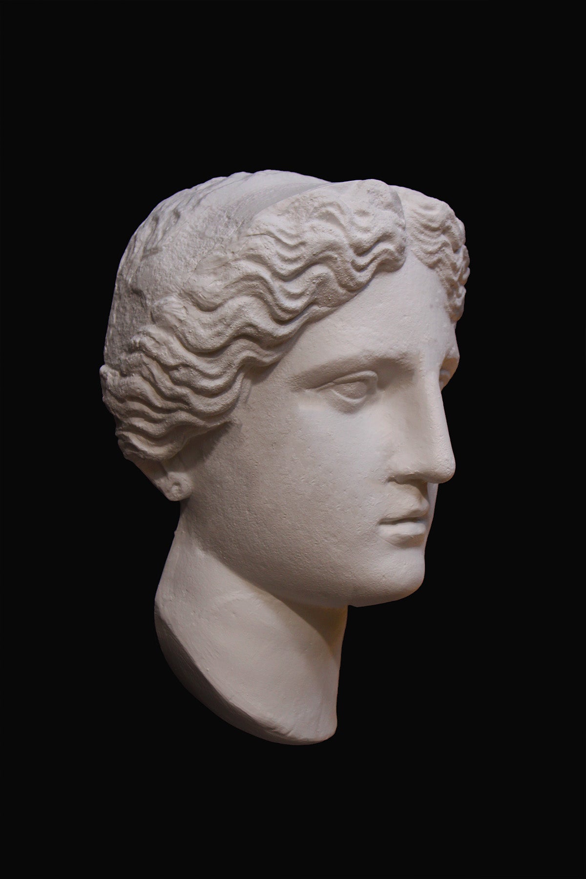 image of plaster cast sculpture mask of female, namely Athena, on a black background