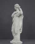 photo of white plaster cast statue of female in robes with left arm raised and holding robe on gray background