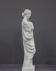 photo of white plaster cast statue of female in robes with left arm raised and holding robe on gray background