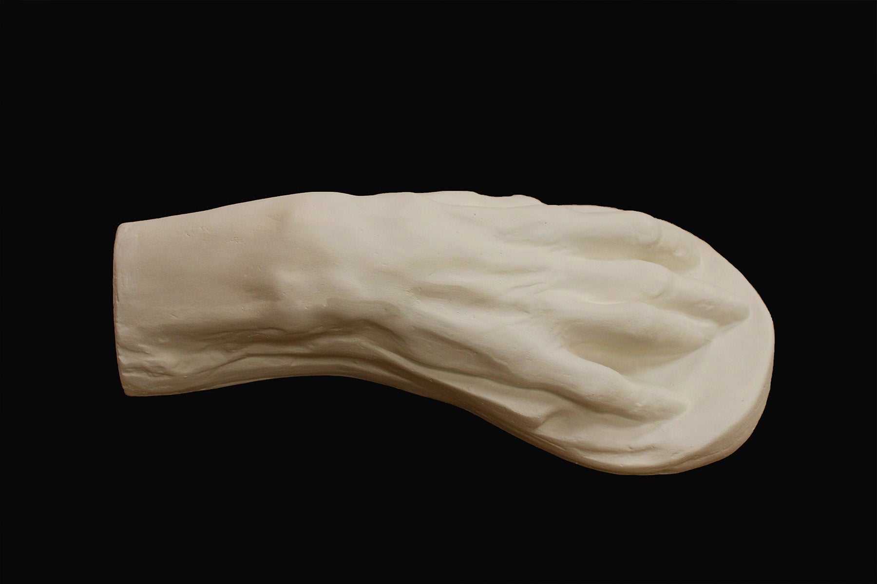 Photo of a white plaster cast of an elderly hand on a black background