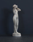 image of a plaster statue of a nude female figure, namely Phryne, on a gray background