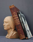 image of a terracotta-colored plaster bust of the well-known Native American Massasoit with books leaning against it on a gray background