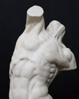 Photo of plaster cast sculpture of flayed male torso and a sculpting tool on a gray surface in front of a black background