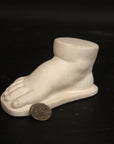 photo of off-white plaster cast sculpture of baby foot against black background