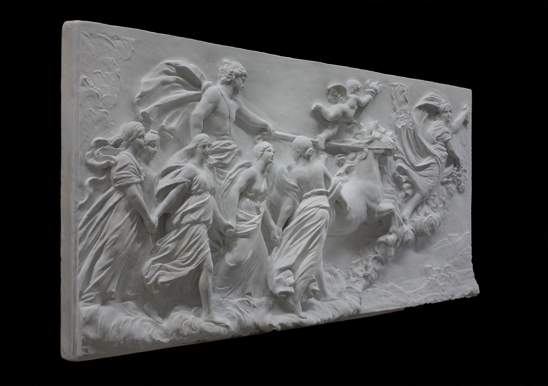 photo of a plaster cast sculpture relief of a woman, namely the goddess Aurora, flying and leading a chariot with a man pulled by horses towards the right while a cherub and other women fill the scene, on a black background