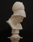 photo of plaster cast sculpture bust of female head, namely the goddess Minerva, with a helmet and looking down and placed on a pedestal with black background