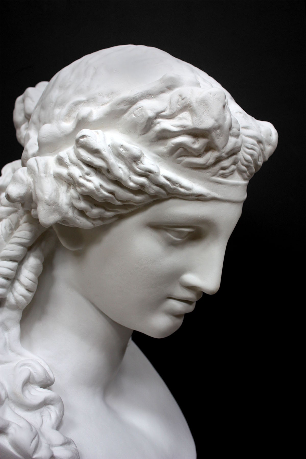 detail photo of plaster cast of sculpture bust of Ariadne or Bacchus with long, curly hair and head band on a gray background