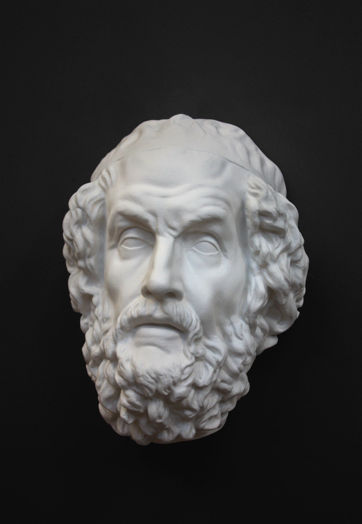 Photo of a white plaster cast mask from a sculpture of Homer on a black background