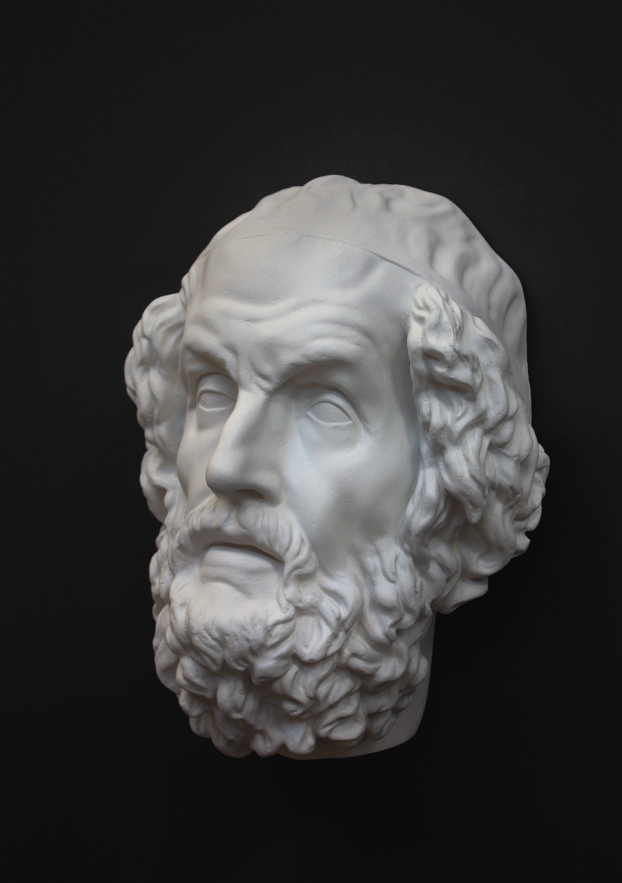 Photo of a white plaster cast mask from a sculpture of Homer on a black background