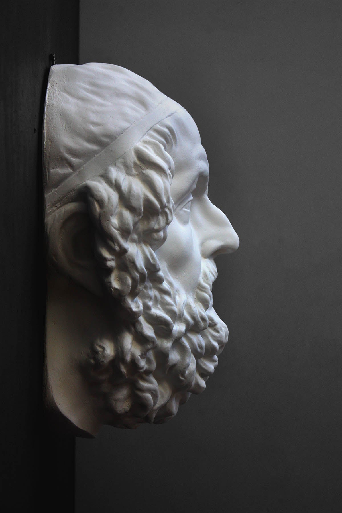 Photo of a white plaster cast mask from a sculpture of Homer on a gray background